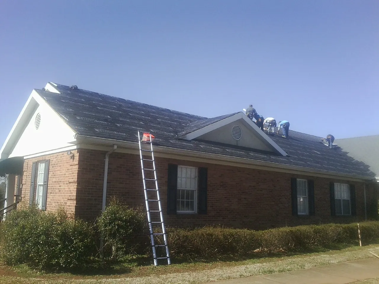 Crew tearing shingles off a brick ranch roof with a ladder set — Metal Roof Repair work by our crew in Russell