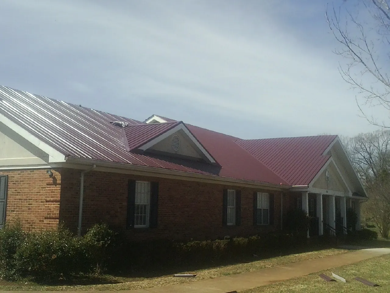 Red metal roof with gabled entries on a long brick building, from a Hail Damage Roof Repair job in Russell