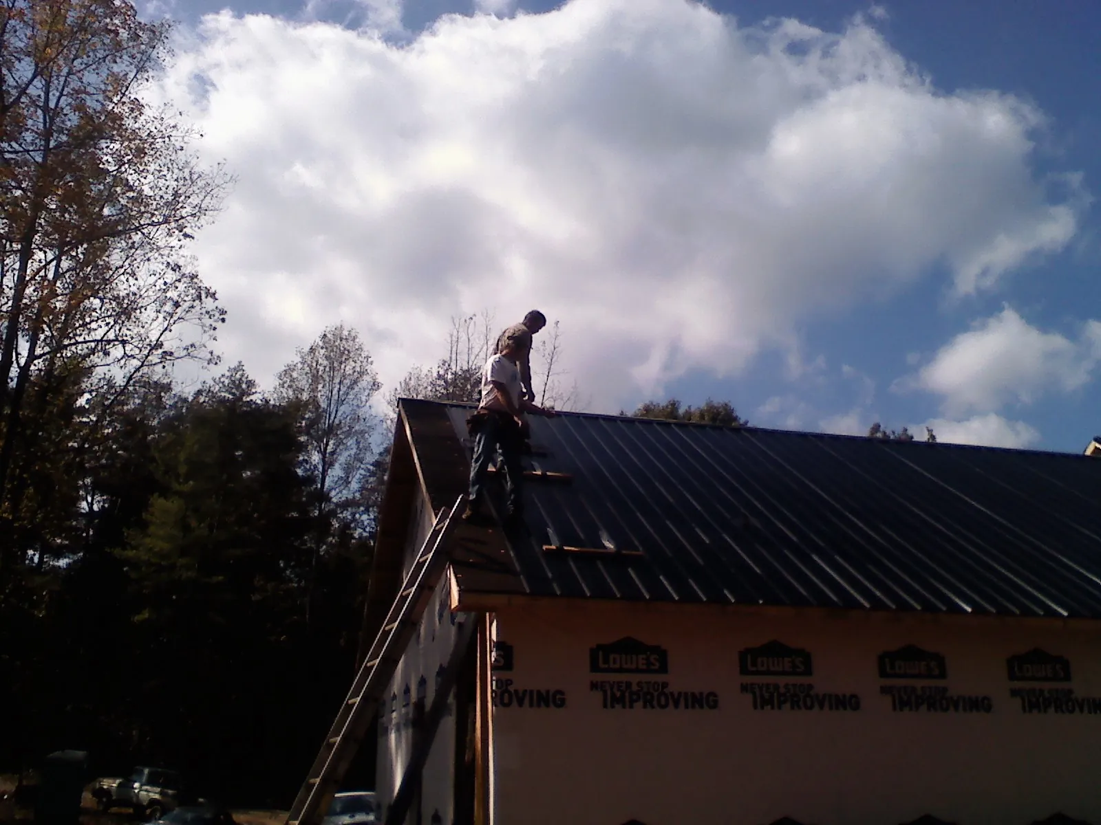 Roofer fastening dark metal panels high against a cloudy sky, from a Roof Inspection job in Russell